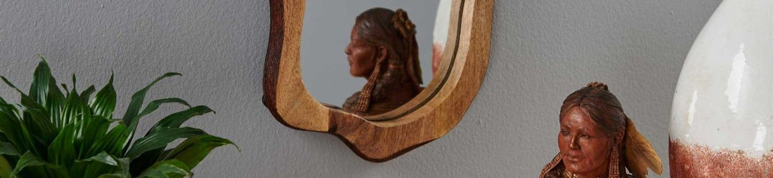 A wooden mirror reflecting a sculpture in front of it.