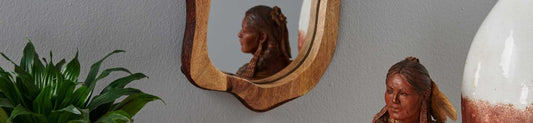 A wooden mirror reflecting a sculpture in front of it.